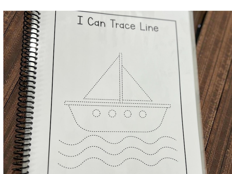 May include: A spiral-bound workbook page with the text "I Can Trace Line." The page features a dotted line drawing of a sailboat with a triangular sail and wavy lines representing water. The image is in black and white.