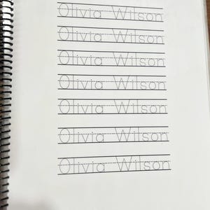 May include: A spiral-bound notebook with lined pages featuring the name "Olivia Wilson" in handwriting practice format. The name is repeated multiple times on each page, with dotted lines for tracing.