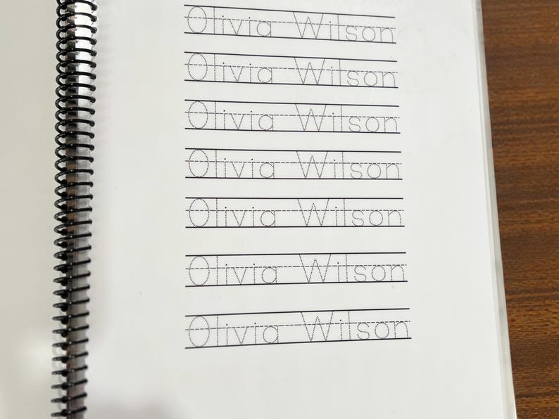 May include: A spiral-bound notebook with lined pages featuring the name "Olivia Wilson" in handwriting practice format. The name is repeated multiple times on each page, with dotted lines for tracing.