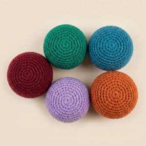 Puede incluir: Una colección de seis bolas hechas a mano, tejidas a ganchillo, en varios colores: burdeos, verde, turquesa, morado y naranja. Las bolas están dispuestas sobre un fondo neutro, mostrando su diseño texturizado en espiral. Estas bolas probablemente se usan para malabares o jugar.