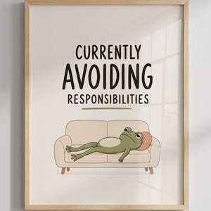 May include: A framed wall art print featuring a light green frog lying on a beige sofa with a small pink pillow. The text above the frog reads CURRENTLY AVOIDING RESPONSIBILITIES in black capital letters with a horizontal line underneath.