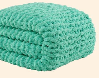 Könnte beinhalten: Eine gefaltete, grob gestrickte Decke in einem weichen, meergrünen Farbton. Die Decke hat ein dickes, strukturiertes Aussehen mit sichtbaren Schlaufen und einem weichen Griff. Die gefalteten Schichten deuten auf einen gemütlichen, warmen Artikel hin, ideal für die Inneneinrichtung.