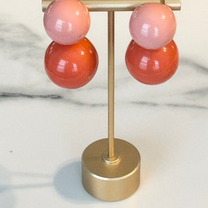 May include: A pair of pink and orange double-layered sphere earrings on a gold stand.