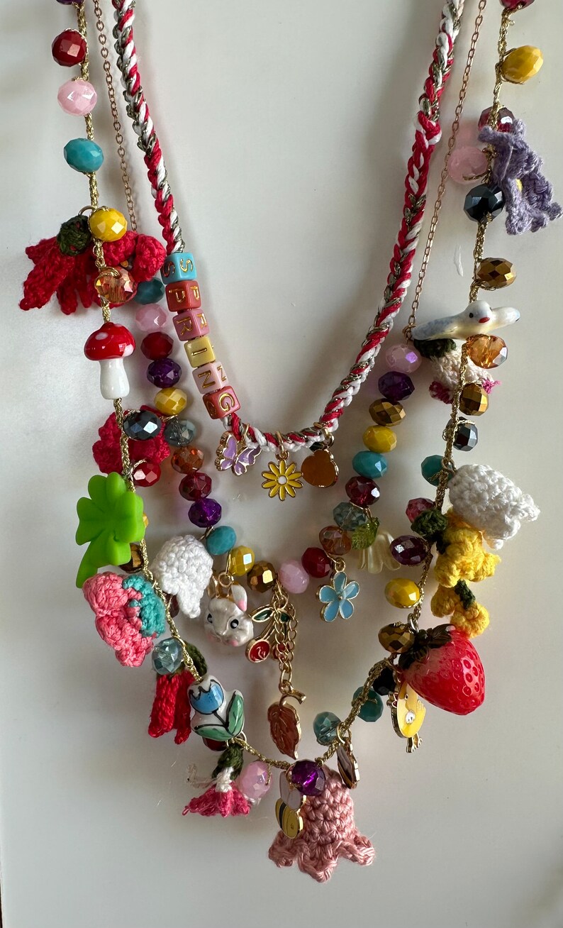 May include: Multi-strand necklace with a variety of colorful beads, charms, and crocheted flowers. The necklace features a charm with the word "SPRING" spelled out in colorful blocks.