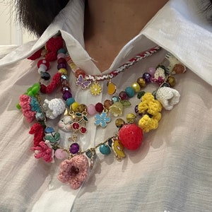 May include: A multi-layered necklace with a variety of colorful charms, including crocheted flowers, a bunny, a cherry, a strawberry, and a butterfly. The necklace is made of beads, string, and metal.