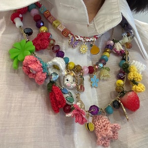 May include: A multi-layered necklace with a variety of charms, including crocheted flowers, a bunny, a strawberry, a bee, and a butterfly. The necklace also features a beaded section with the word "SPRING" spelled out in colorful beads.