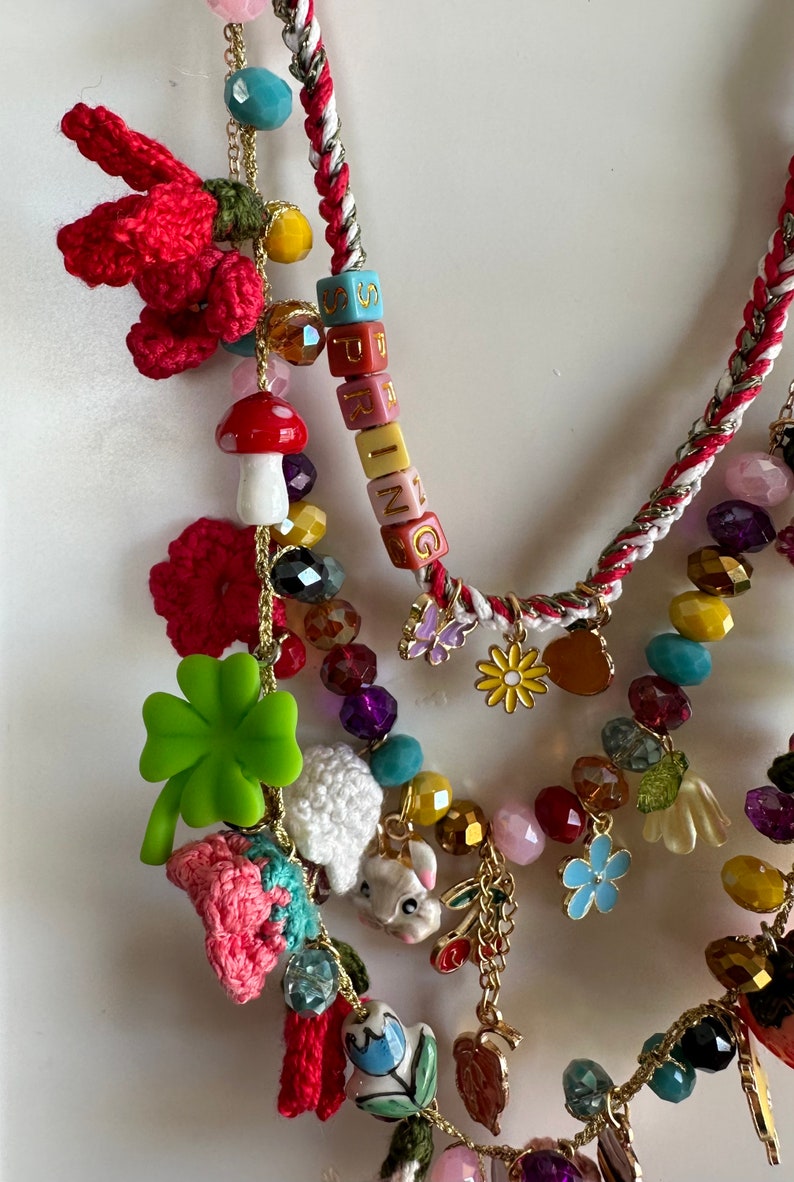 May include: Multi-strand necklace with colorful beads, charms, and crocheted flowers. The necklace features a charm with the word "SPRING" spelled out in colorful blocks.