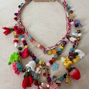 May include: Multi-layered necklace with a spring theme. It features crocheted flowers, a bunny charm, a strawberry charm, and beads in various colors. The necklace also includes a tag that says "Spring".
