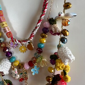 May include: A multi-strand necklace with colorful beads, charms, and crocheted elements. The necklace features a variety of charms, including flowers, birds, strawberries, and a bunny. The necklace also includes a beaded section with the word "SPRING" spelled out in colorful letters.