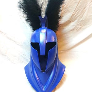 May include: A blue helmet with a black feather plume. The helmet has a pointed top and a face mask with a narrow opening for the eyes.