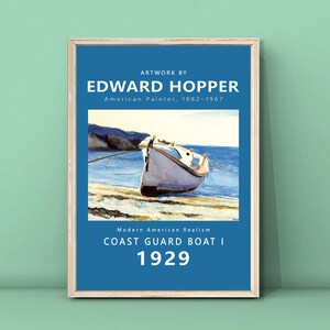 Op de afbeelding: Een ingelijste print van Edward Hopper's "Coast Guard Boat I" uit 1929. Het kunstwerk toont een witte boot op een strand met een blauwe zee en lucht. Tekst bevat de naam van de kunstenaar en "Modern American Realism."