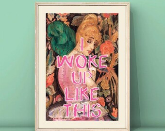 May include: A framed print of a painting of a woman with blonde hair in a pink dress. The text "I woke up like this" is written in pink letters over the image.
