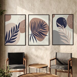 May include: Three framed abstract art prints with a minimalist design featuring stylised leaves in shades of brown, blue, and grey on a white background.