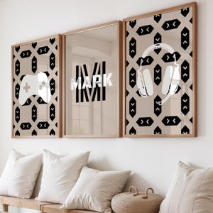 Pode incluir: Três quadros de parede com fundo bege claro e um padrão geométrico preto repetitivo. O quadro da esquerda apresenta um comando de jogo branco, o central exibe o nome MARK em branco e o da direita mostra auscultadores brancos.