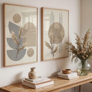 Puede incluir: Dos impresiones artísticas enmarcadas con patrones abstractos y una paleta de colores neutros. Cada impresión presenta formas geométricas, círculos y semicírculos, y elementos botánicos en beige, marrón y negro. Se exhiben sobre una mesa de madera.
