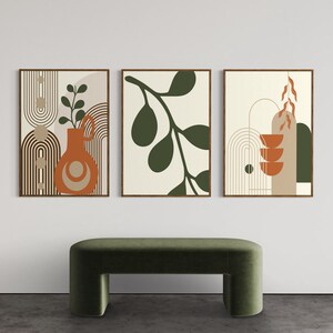 Könnte beinhalten: Drei abstrakte Kunstdrucke mit minimalistischem Design, die geometrische Formen, Blätter und eine Vase in Braun-, Grün- und Orangetönen zeigen. Die Drucke sind in Holz gerahmt und an einer weißen Wand aufgehängt.