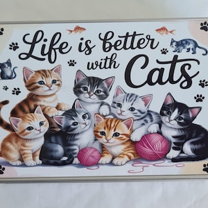 Könnte beinhalten: Rechteckige Metallbox mit dem Schriftzug "Life is better with Cats". Das Bild zeigt eine Gruppe von Cartoon-Kätzchen in verschiedenen Farben, mit Pfotenabdrücken und Fischmotiven. Ein rosa Wollknäuel ist ebenfalls abgebildet.