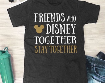 以下が含まれることがあります： 「FRIENDS WHO DISNEY TOGETHER STAY TOGETHER」の文字が白と金色の文字でプリントされた濃いグレーのTシャツ。金色のミッキーマウスの頭のグラフィックが「DISNEY」という単語の上にあります。サングラス、緑色のウォーターボトル、ジーンズも画像にあります。