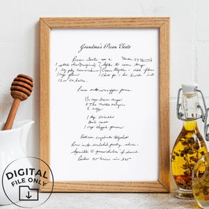 Peut inclure: Une impression encadrée d'une recette manuscrite pour les "Tartelettes aux pacanes de grand-mère". La recette est à l'encre noire sur papier blanc, encadrée en bois clair. Un pichet blanc avec des ustensiles en bois et deux bouteilles en verre avec de l'huile et des herbes sont au premier plan.