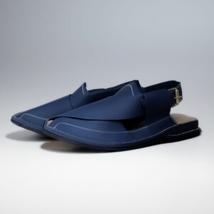 May include: A pair of dark blue leather sandals with a strap and buckle. The sandals have a pointed toe and a flat sole.