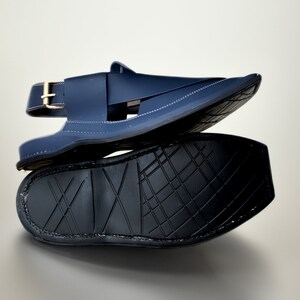 May include: A pair of dark blue leather sandals with a buckle strap and a textured black sole.