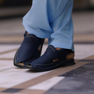 May include: A pair of dark blue leather sandals with a stitched design. The sandals have a strap that goes around the ankle and a buckle closure.