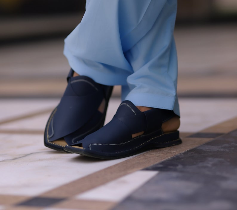 May include: A pair of dark blue leather sandals with a stitched design. The sandals have a strap that goes around the ankle and a buckle closure.