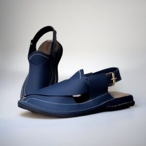 May include: A pair of dark blue leather sandals with a buckle strap and white stitching. The sandals have a pointed toe and a flat sole.