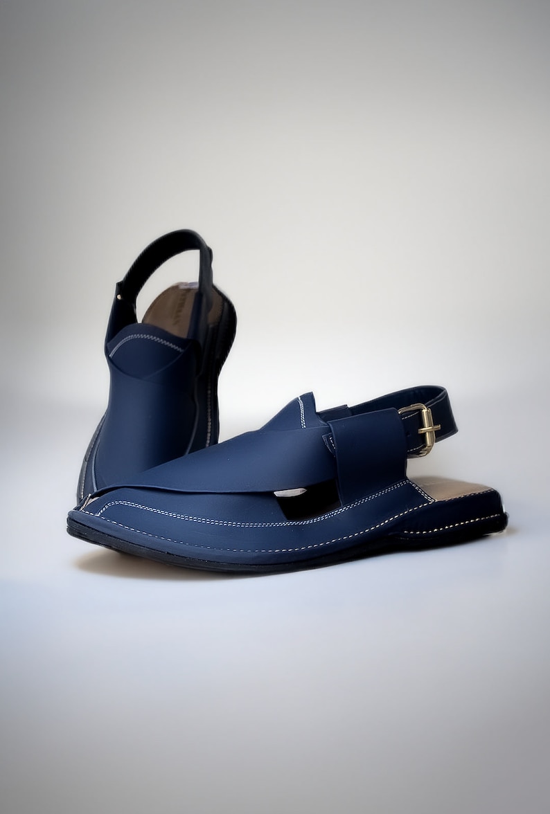May include: A pair of dark blue leather sandals with a buckle strap and white stitching. The sandals have a pointed toe and a flat sole.