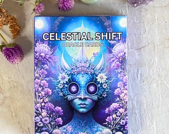 May include: A deck of Celestial Shift Oracle Cards with a blue and purple design featuring a masked figure with flowers and a starry background. The text on the box reads "Celestial Shift Oracle Cards".