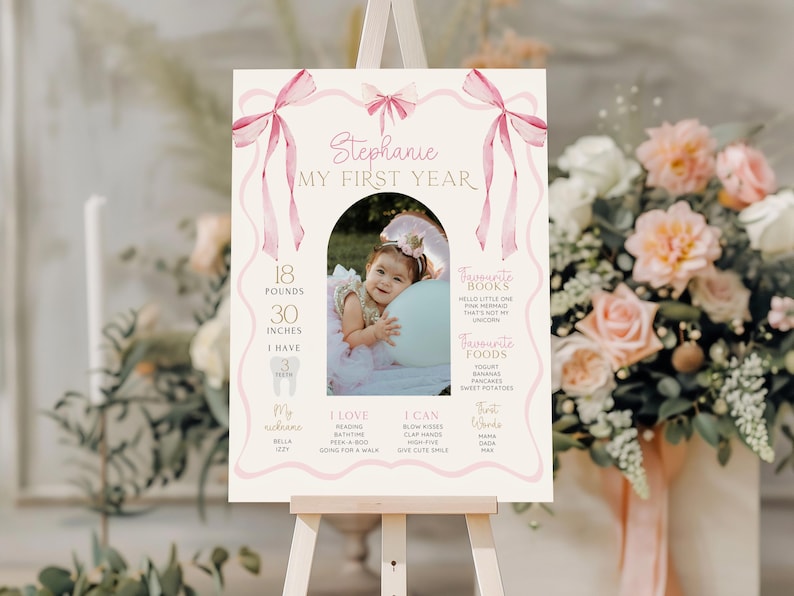 May include: A personalized first birthday sign on an easel. The sign features a photo of a baby, with stats including 18 pounds and 30 inches. The sign is decorated with pink bows and ribbons, and includes the text "Stephanie MY FIRST YEAR."