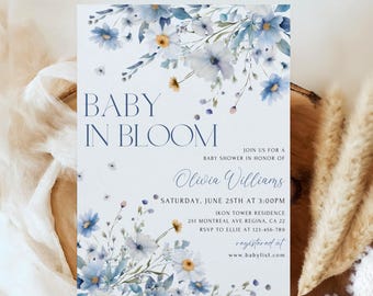 Puede incluir: Una invitación a un baby shower con un diseño floral de acuarela en tonos azules y amarillos. El texto dice "Baby in Bloom" e incluye el nombre "Olivia Williams", la fecha y hora de la ducha, y la ubicación. La invitación también incluye la información de RSVP y el sitio web donde los invitados pueden registrarse.