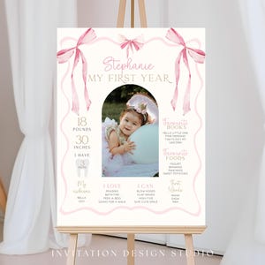 May include: A personalized first birthday sign on an easel. The sign features a photo of a baby girl, pink bows, and text including the baby's name, measurements (18 pounds, 30 inches), and favorite things.