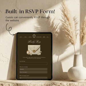 May include: A tablet screen displaying a wedding website with a built-in RSVP form. The dark brown interface features the text "Kindly RSVP" above an envelope graphic, a pearl brooch, and heart charms, with fields for name and attendance status.