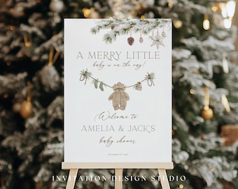 May include: A baby shower sign on an easel with the text "A Merry Little Baby is on the Way!" and "Welcome to Amelia & Jack's baby shower." The sign has a winter theme with a knitted baby outfit.