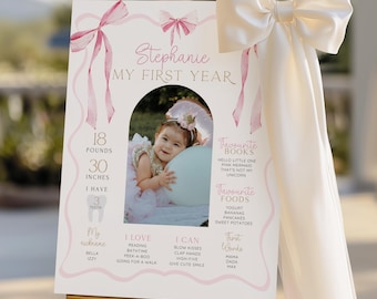 Può includere: Un cartello personalizzato per il primo compleanno con la foto di una bambina. Il cartello include il nome del bambino, il peso (8,2 kg), l'altezza (76 cm) e le sue cose preferite. Fiocchi e nastri rosa decorano il cartello.