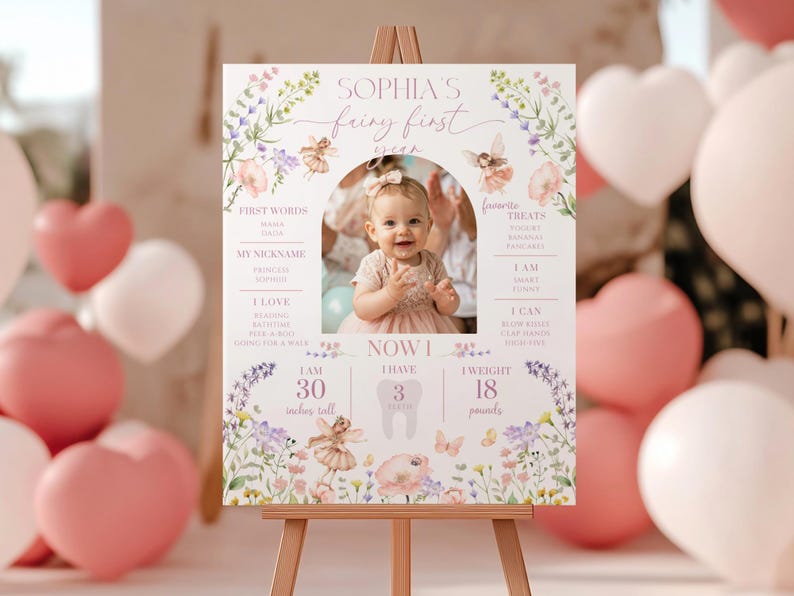 May include: A personalized sign on an easel, featuring a photo of a baby girl. The sign includes the text "Sophia's Fairy First Year," along with details like height (30 inches), weight (18 pounds), and favorite treats. Floral and fairy illustrations decorate the sign.