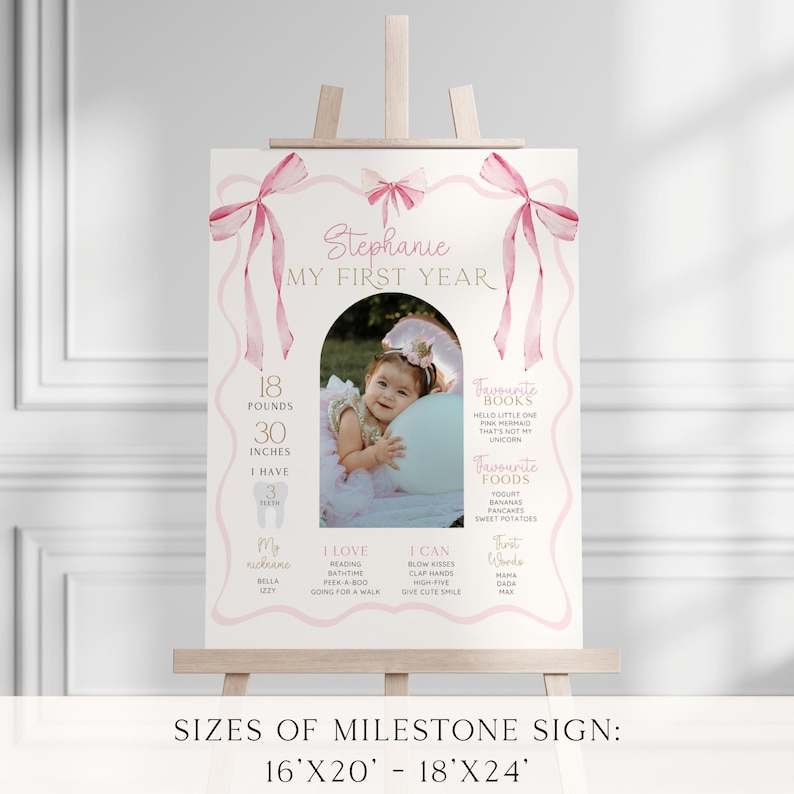 May include: A pink and white milestone sign on a wooden easel. The sign features a photo of a baby, pink bows, and text that reads "Stephanie MY FIRST YEAR." It lists the baby's weight as 18 pounds and height as 30 inches.
