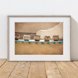 May include: Five colorful ceramic pots with intricate designs sit on a blue shelf against a textured tan wall. The pots are decorated with yellow, blue, red, and green patterns.