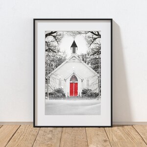 K&ouml;nnte beinhalten: Ein Schwarzwei&szlig;foto einer wei&szlig;en Kirche mit roten T&uuml;ren in einer verschneiten Umgebung. Die Kirche hat einen Kirchturm und ist von B&auml;umen umgeben. Der Schnee f&auml;llt und ein Weg f&uuml;hrt zur Kirche.
