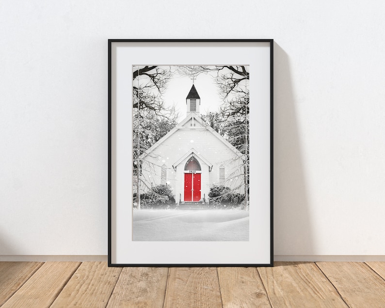 K&ouml;nnte beinhalten: Ein Schwarzwei&szlig;foto einer wei&szlig;en Kirche mit roten T&uuml;ren in einer verschneiten Umgebung. Die Kirche hat einen Kirchturm und ist von B&auml;umen umgeben. Der Schnee f&auml;llt und ein Weg f&uuml;hrt zur Kirche.
