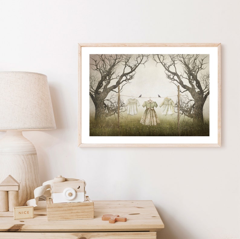 May include: A framed print of a misty forest scene with three white dresses hanging on a clothesline between two trees. The dresses are slightly faded and have a vintage feel. Three small birds are perched on the line.
