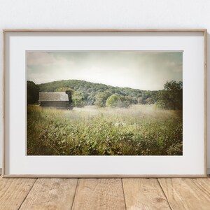 May include: A rustic wooden cabin sits in a field of wildflowers, with a rolling green hill in the background. The scene is bathed in a soft, hazy light, creating a dreamy atmosphere.