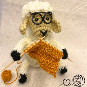 Puede incluir: Una oveja de ganchillo hecha a mano con gafas de montura negra, tejiendo con hilo naranja. La oveja tiene un cuerpo color crema, pezuñas negras y sostiene agujas de tejer. Una bola de hilo naranja está cerca. La imagen incluye el texto "@easyintrameandcrochetclass".