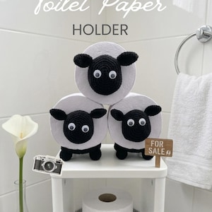 Puede incluir: Un portarrollos de papel higiénico con tres rollos de papel blanco decorados con cabezas, orejas y patas de oveja tejidas en crochet negro, con ojos móviles. El texto dice Toilet Paper HOLDER, FRIENDLY PATTERN y un cartel FOR SALE.