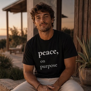 Könnte beinhalten: Ein schwarzes Kurzarm-T-Shirt mit dem weißen Schriftzug "peace, on purpose" auf der Vorderseite. Das Shirt hat einen Rundhalsausschnitt und eine normale Passform, gefertigt aus einem einfarbigen schwarzen Stoff, der sich vom weißen Text abhebt.