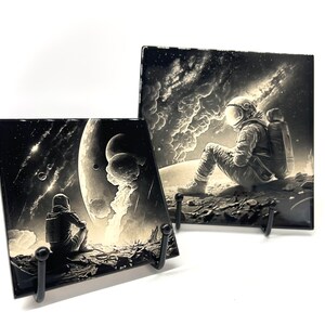 May include: Two black and white ceramic tiles with astronaut illustrations. The first tile shows an astronaut sitting on a planet with a large moon in the background. The second tile shows an astronaut looking up at a starry sky.
