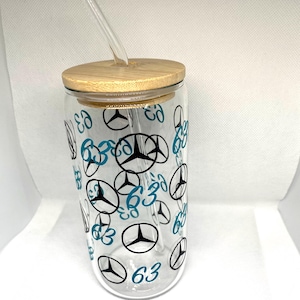 K&ouml;nnte beinhalten: Ein durchsichtiger Glasbecher mit Bambusdeckel und Glasstrohhalm, der mit einem sich wiederholenden Muster aus schwarzen Mercedes-Benz-Logos und der t&uuml;rkisfarbenen Zahl 63 auf der Au&szlig;enseite des zylindrischen Trinkgef&auml;&szlig;es bedruckt ist.
