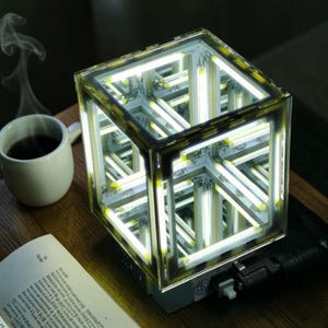 May include: A white ceramic mug with a black handle and the text "But first, coffee" in a black, handwritten-style font. The mug is on a white surface.