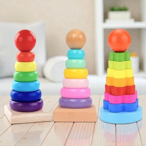 Puede incluir: Tres juguetes de apilamiento de madera coloridos. Cada juguete tiene una forma de base diferente y una serie de anillos graduados en colores del arcoíris. Los juguetes están rematados con una esfera de madera. Un juguete divertido y educativo para niños.